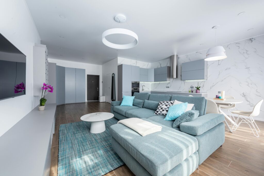 Interior of modern apartment with couch in front of TV on wall near table and chairs next to open kitchen under lamps